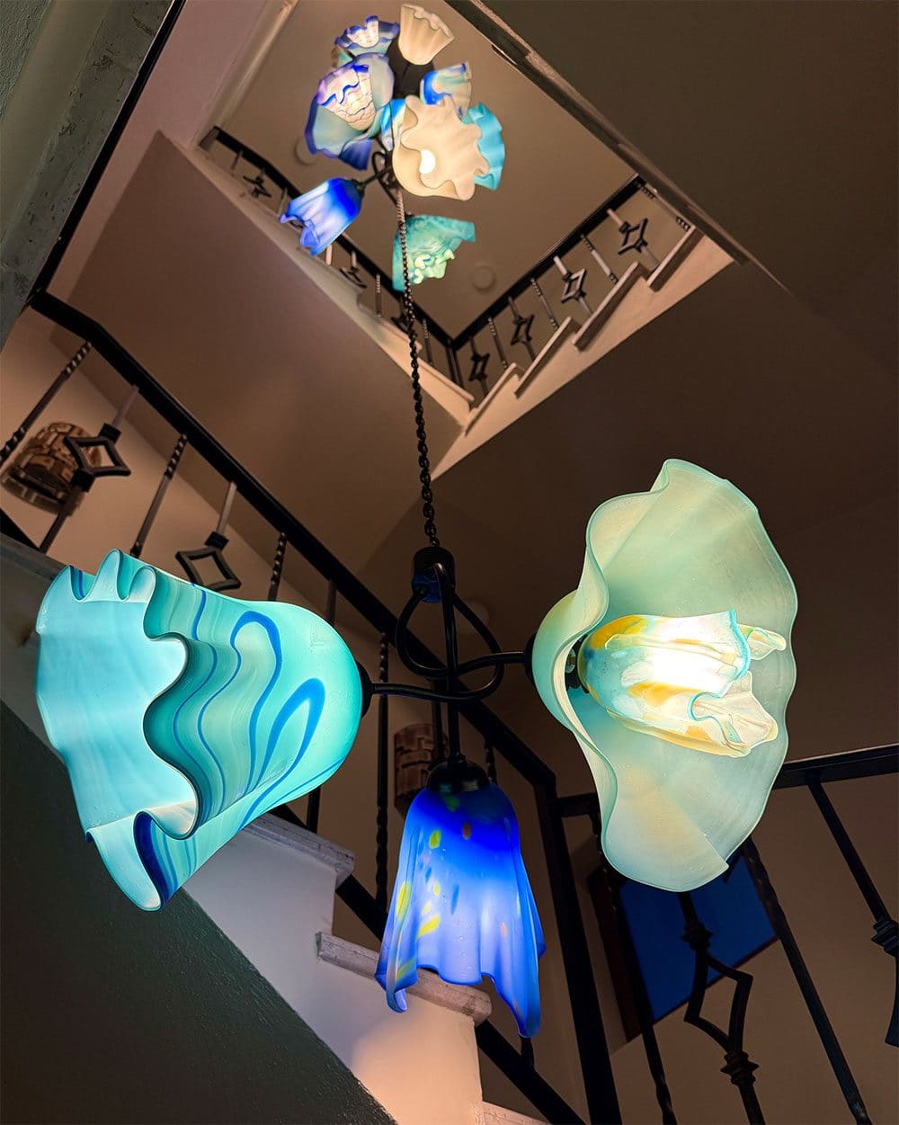 Looking up at a multi-level handblown glass chandelier, ruffled shades in turquoise, blue and cream on a wrought iron frame