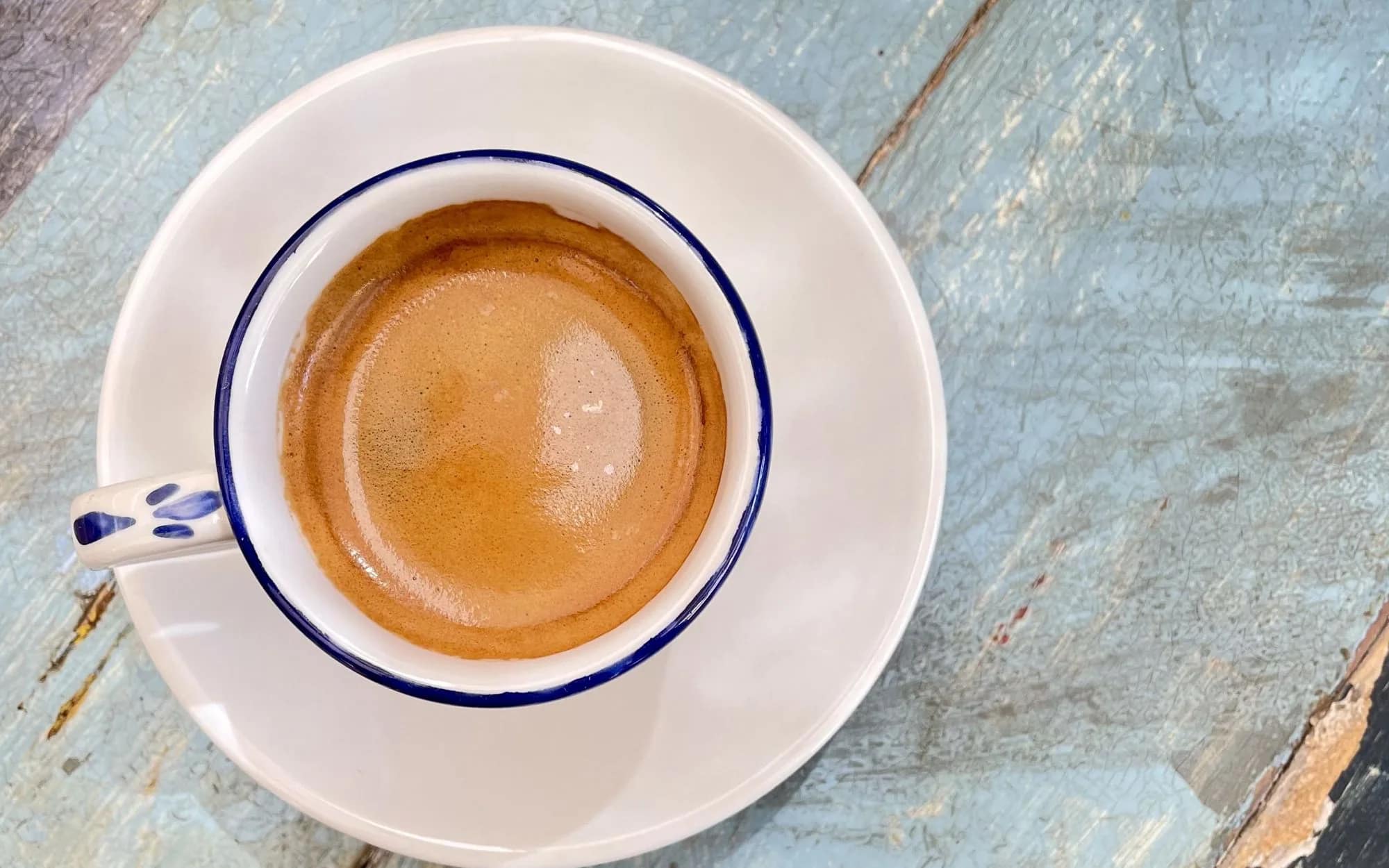 An espresso in a blue-rimmed cup on a weathered blue wooden table, seen from above