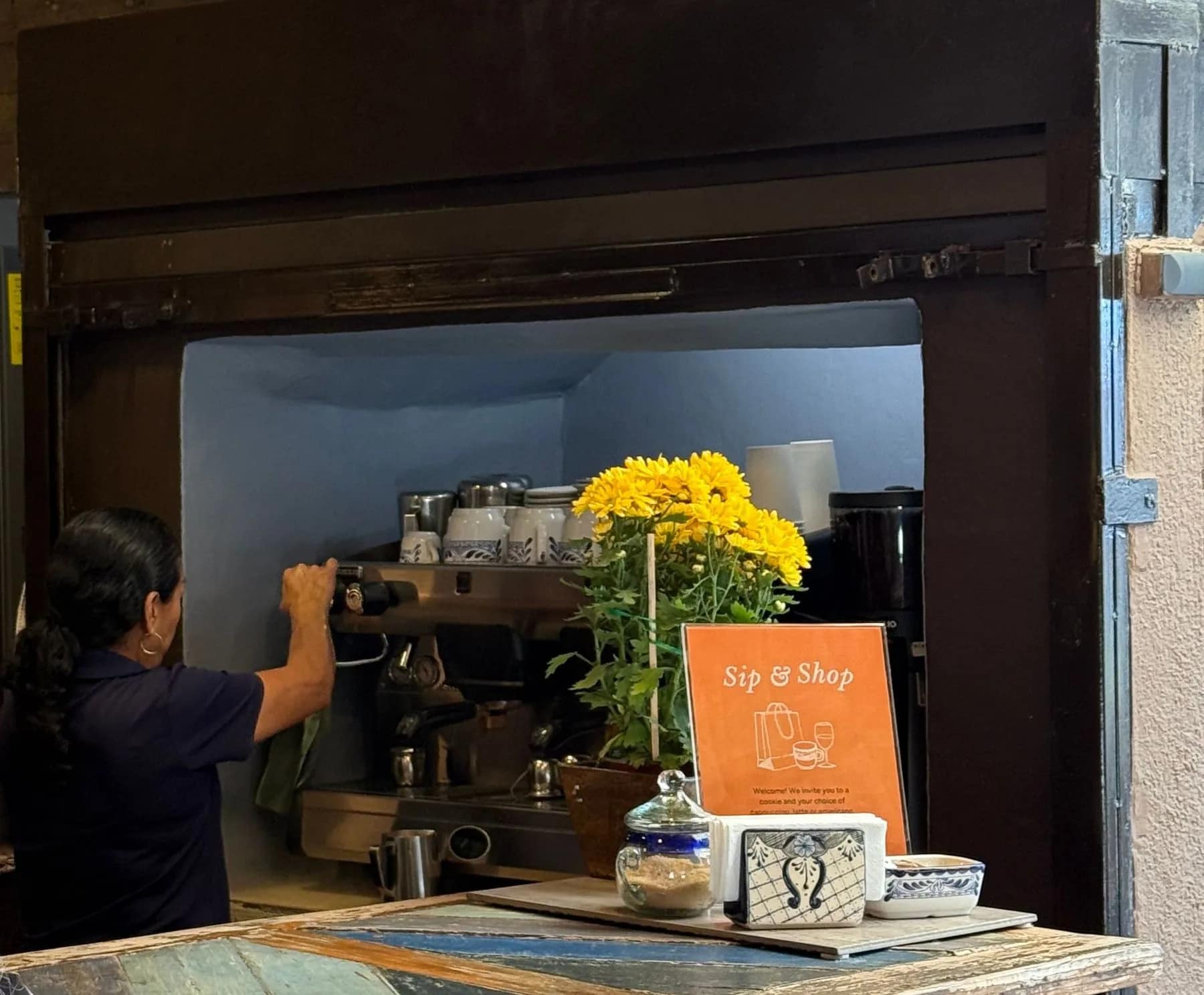 A barista at the espresso machine behind the Chalala counter, yellow flowers and a Sip & Shop sign on the bar