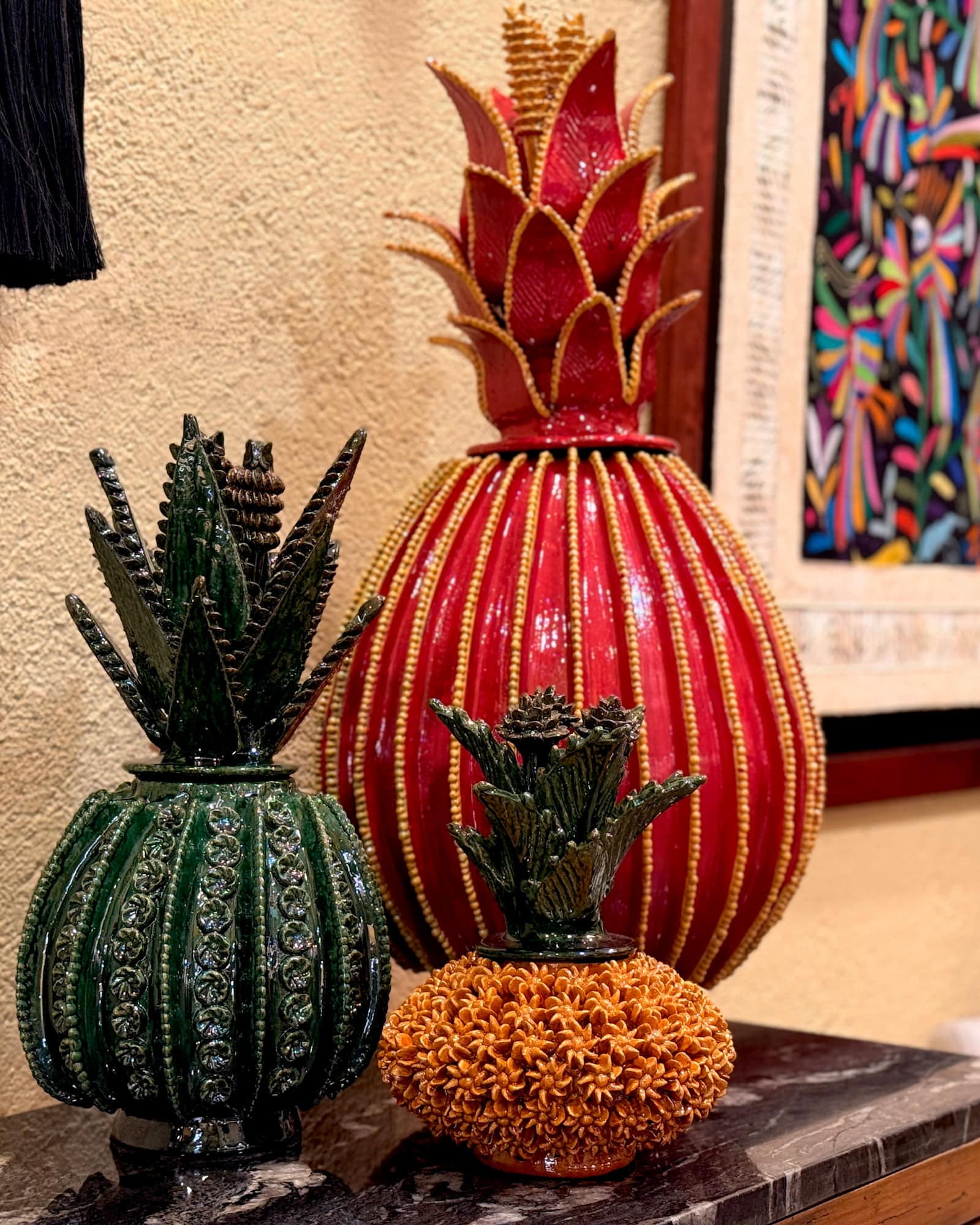 Glazed ceramic pineapple and agave vessels in deep red and forest green on a marble ledge