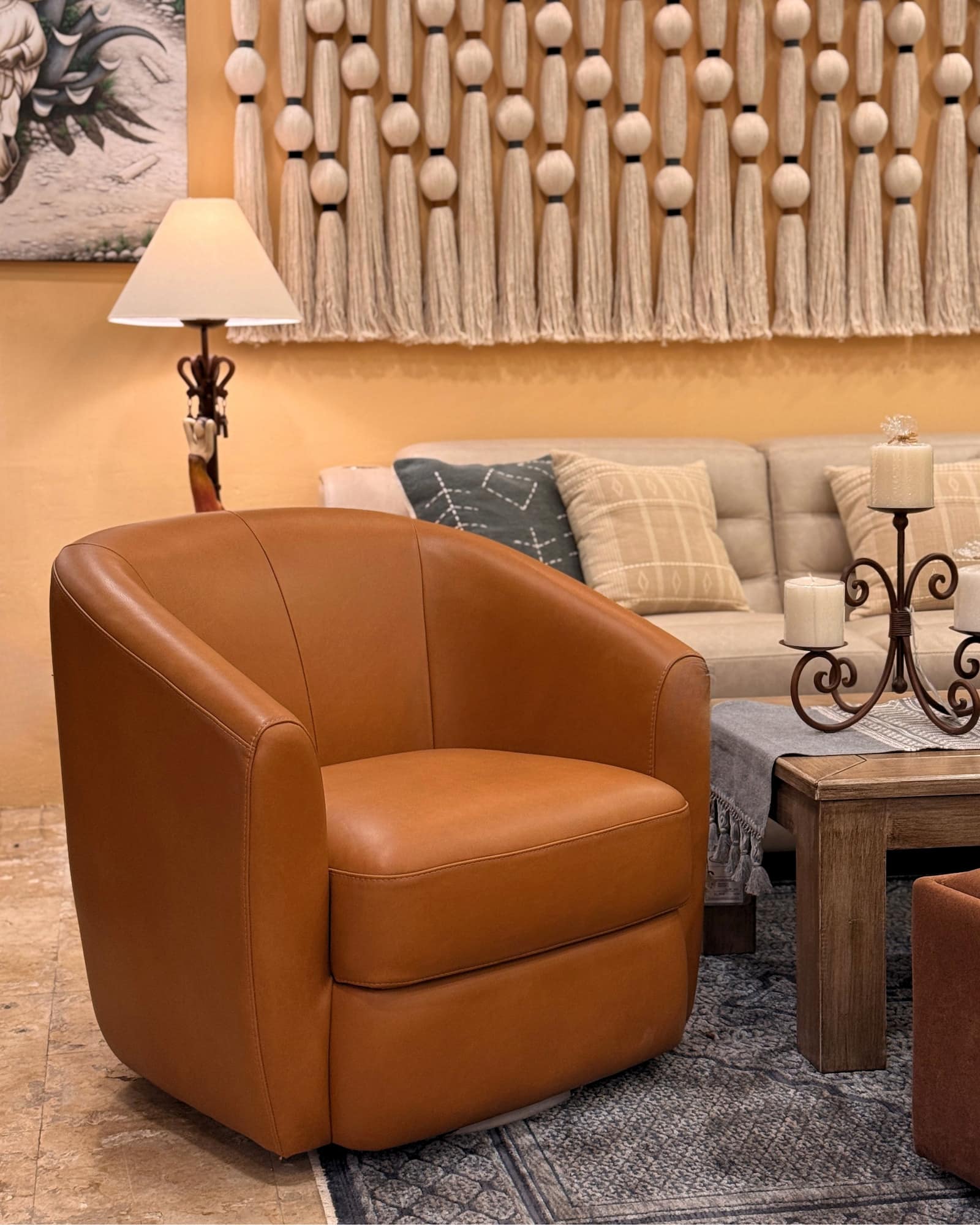 Tan leather swivel barrel chair in front of a linen sofa and a knotted cotton wall hanging