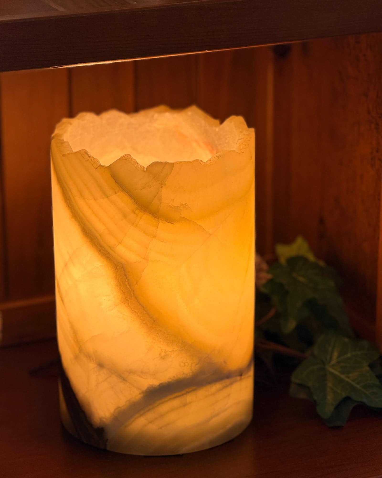 Hand-cut onyx cylinder lamp glowing amber on a walnut shelf