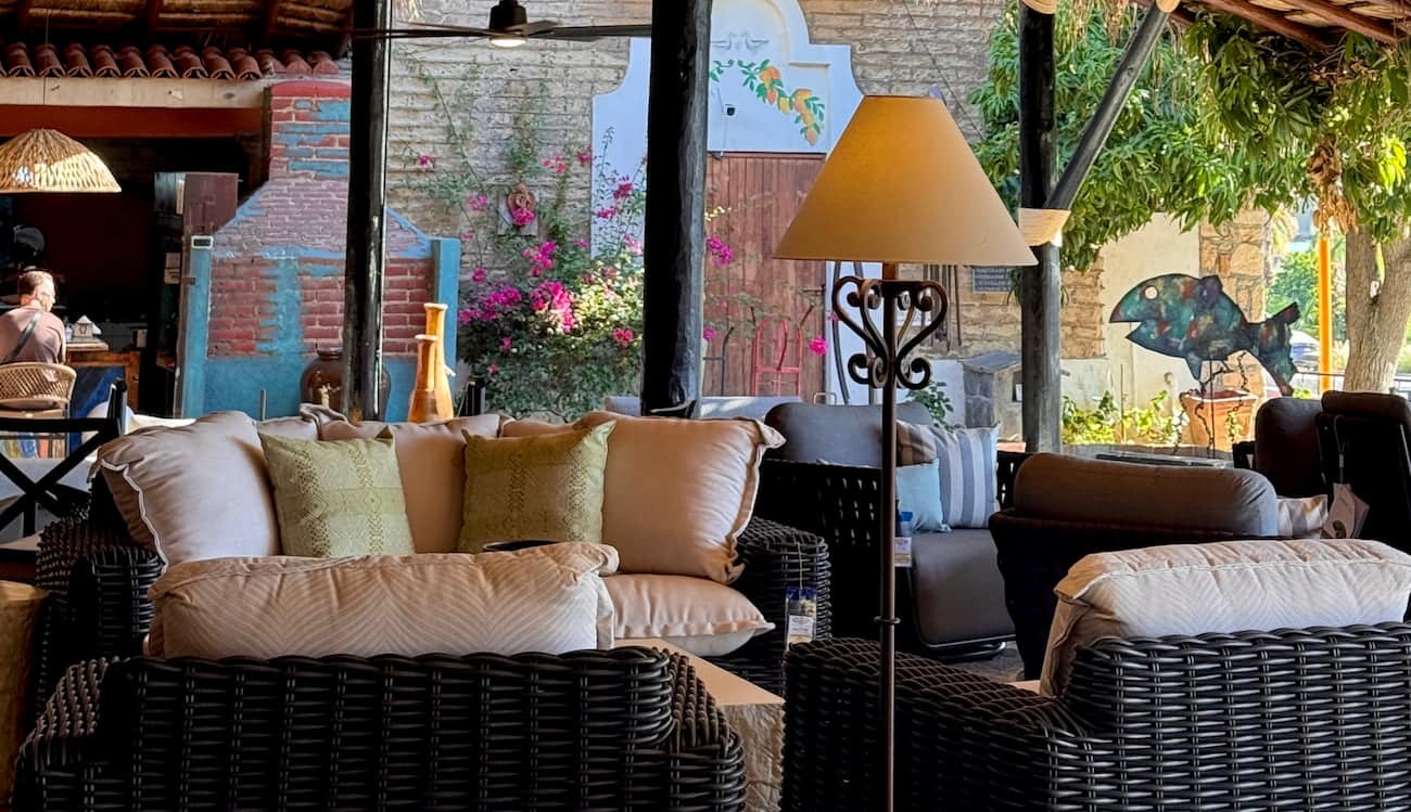 Covered patio with deep woven outdoor seating, cushions and a garden of flowering trees beyond