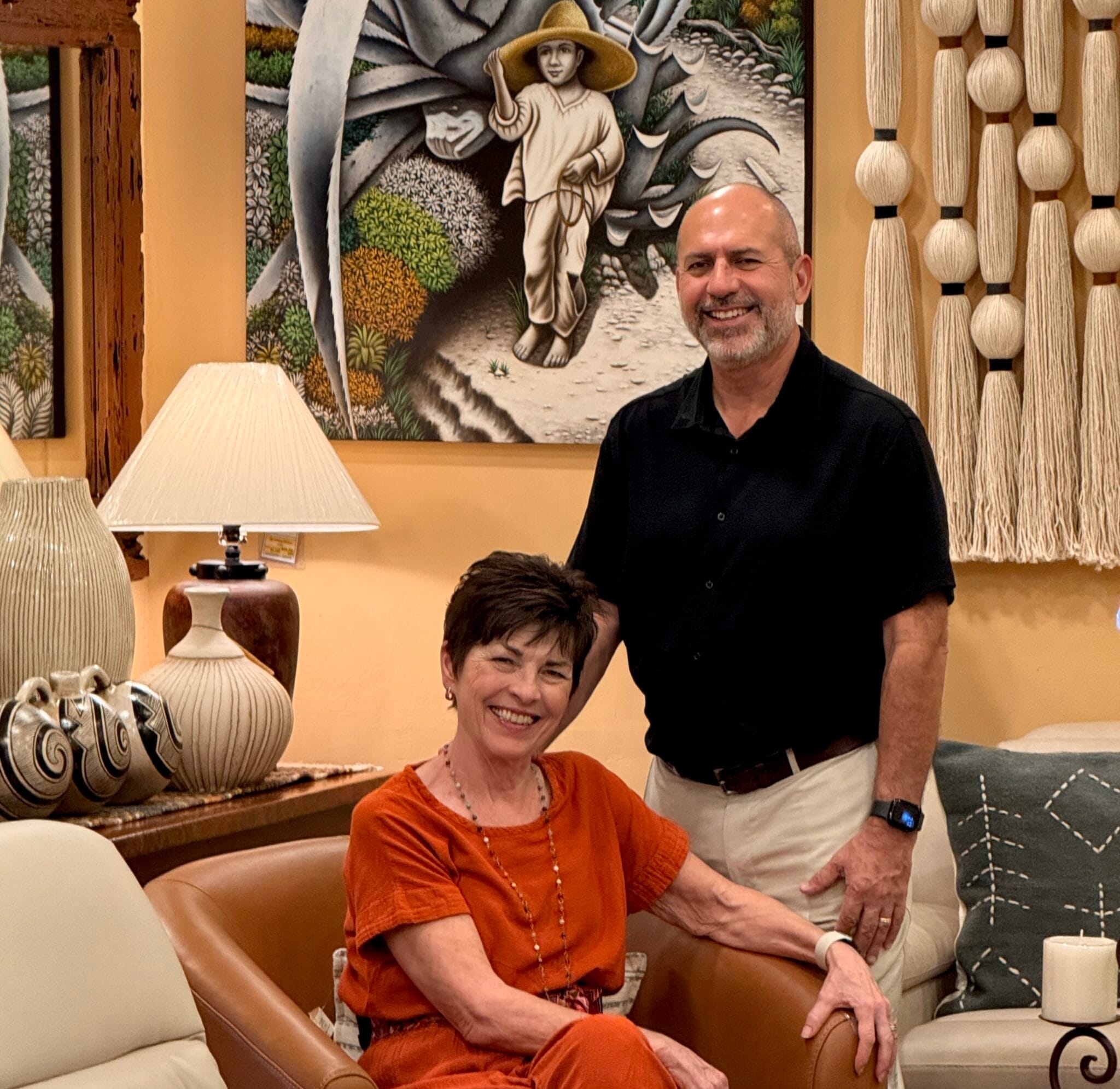 Casa Bonita founders Marsha and Jorge in the showroom, seated and standing beside a carved lamp and framed artwork