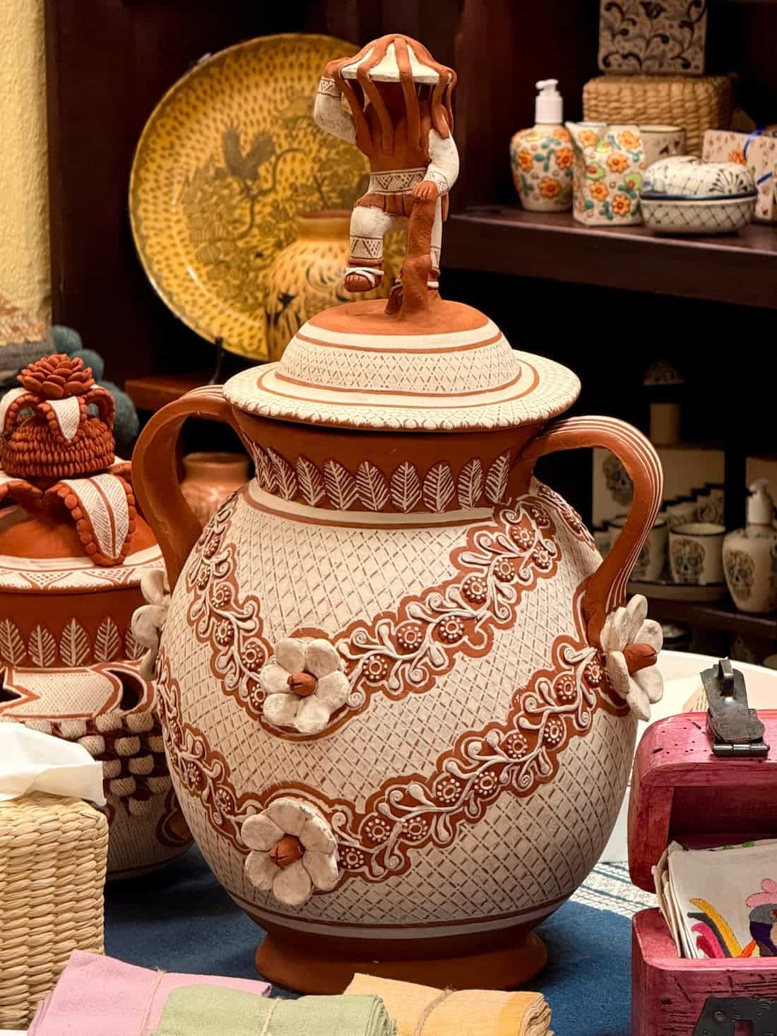A two-handled Patambán urn banded with white vine work and applied flowers, topped by a small modeled figure
