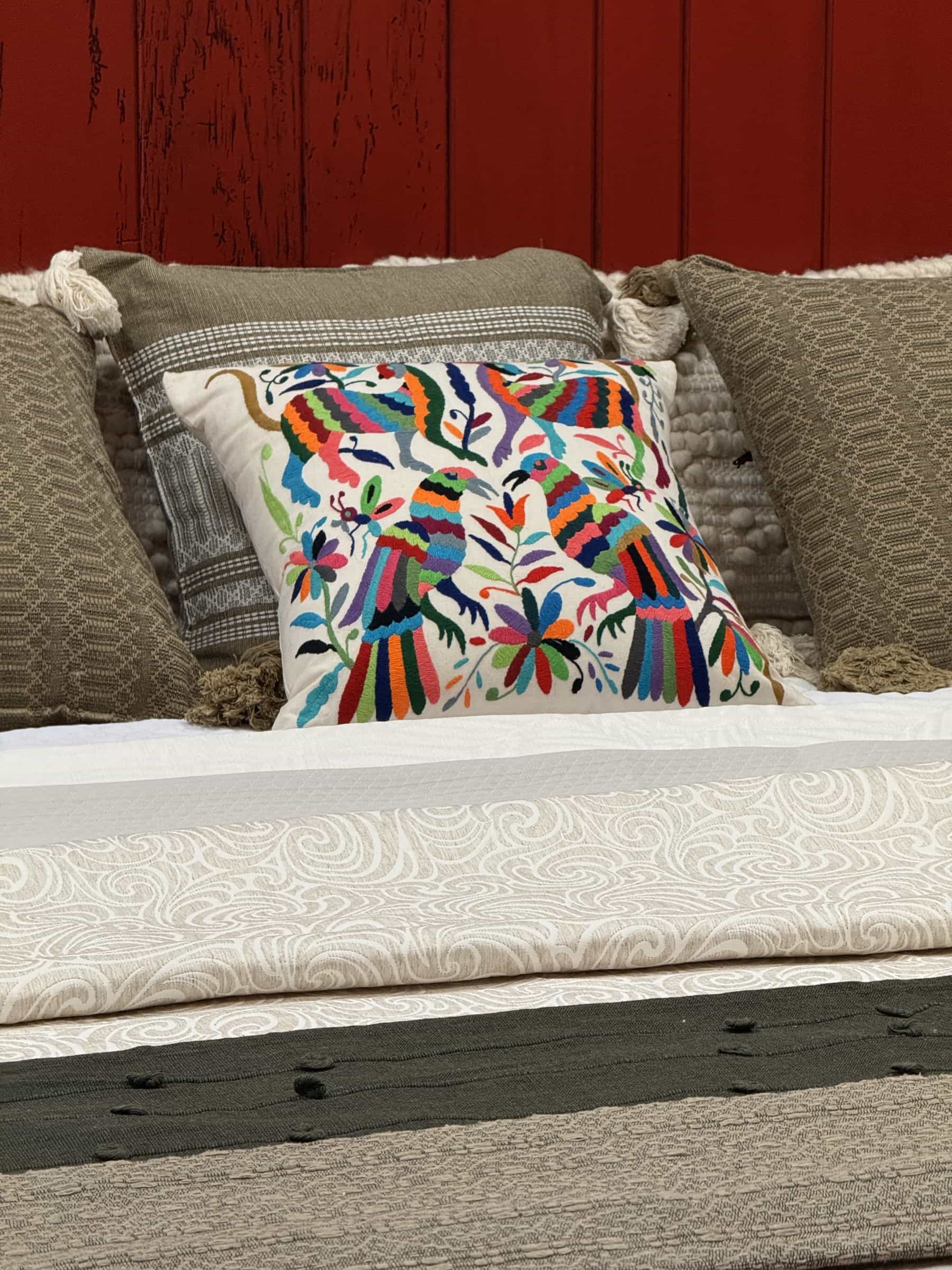 A multicolored Otomí embroidered pillow on a bed layered with woven coverlets